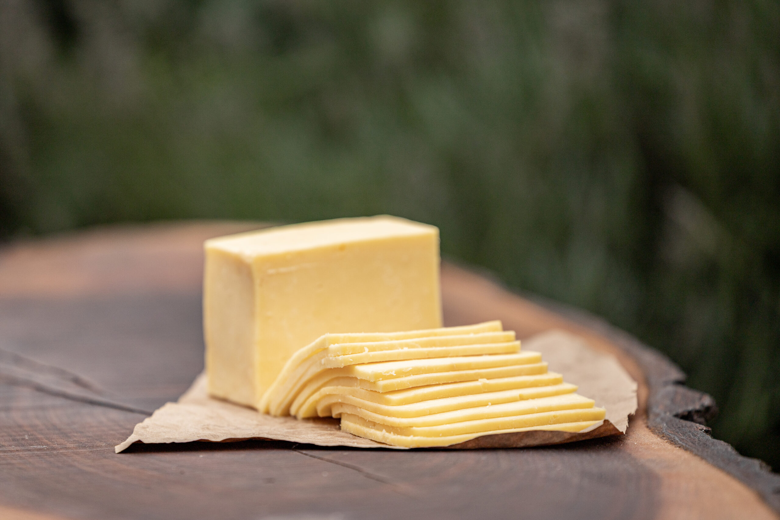 Block of butter on parchment paper with sliced pieces, placed on a wooden cutting board, surrounded by a light-colored cloth and a knife. Ideal for cooking and baking.