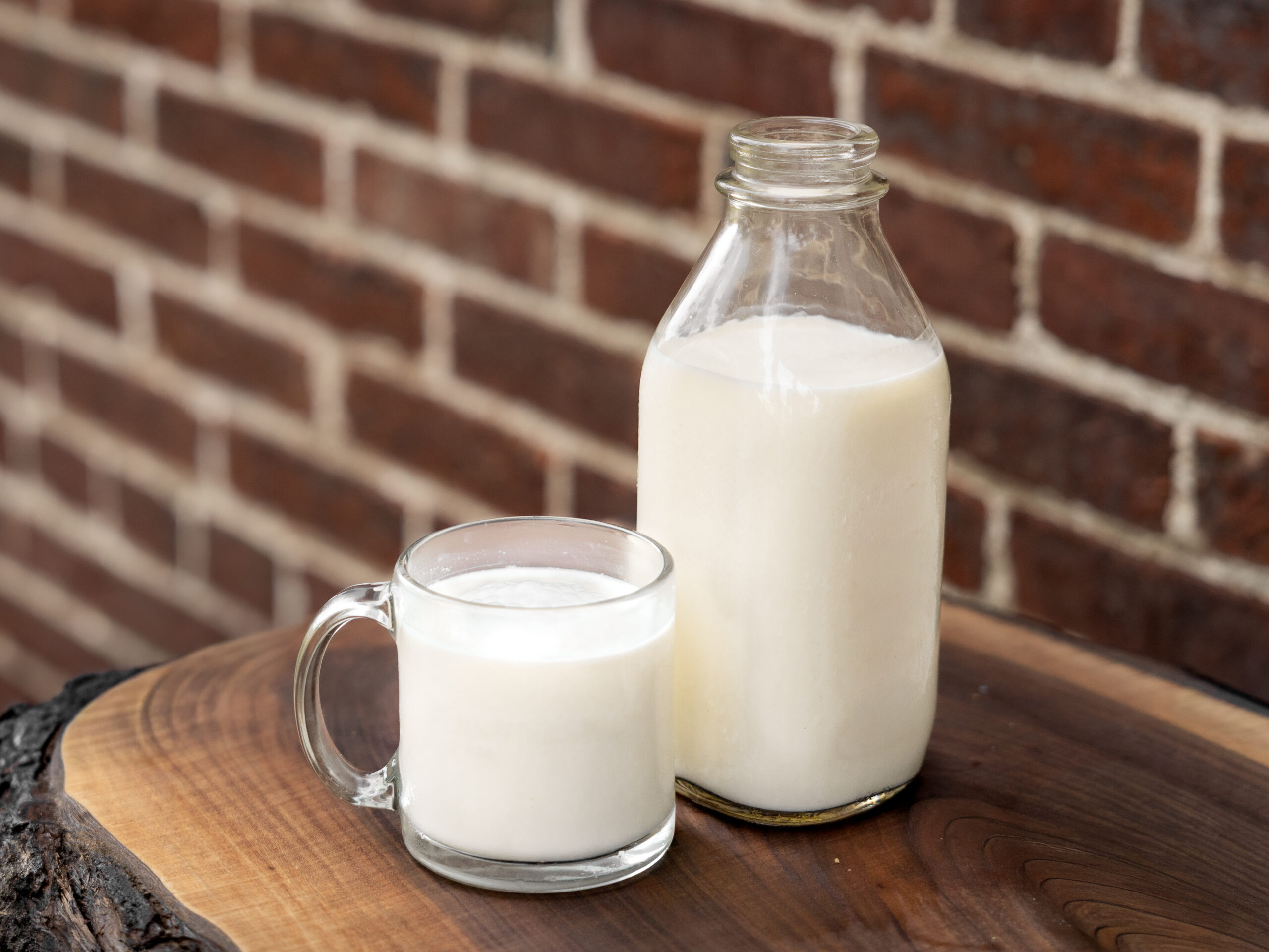 Person holding a glass milk bottle tied with twine, wearing a plaid shirt, with a blurred green garden background. Ideal for topics on homemade dairy, sustainability, or organic farming.